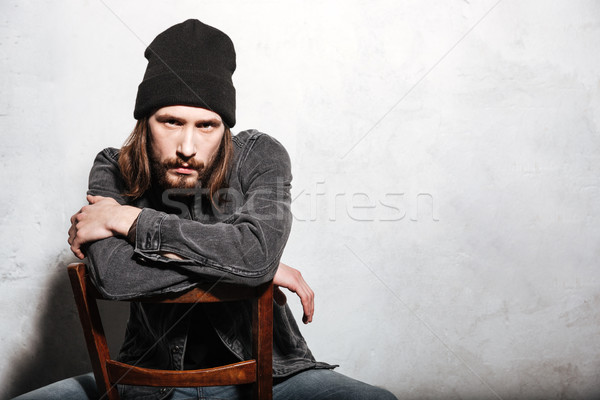 Young bearded man sitting on chair and looking at camera Stock photo © deandrobot