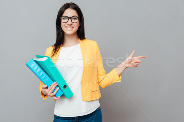 Young pretty woman holding folders and ponting to copyspace Stock photo © deandrobot