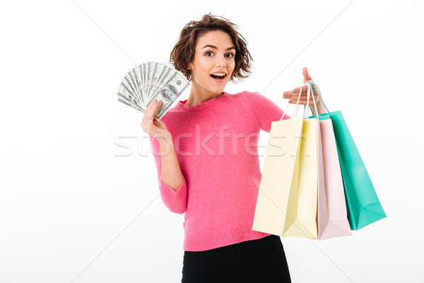 Smiling young lady standing isolated with shopping bags and money. Stock photo © deandrobot