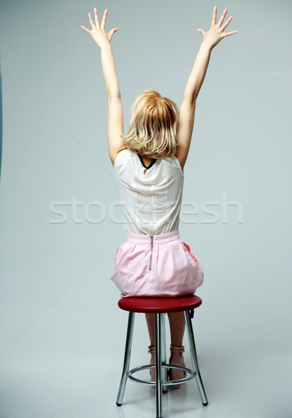 back view portrait of a young woman sitting with hands raised up on gray background Stock photo © deandrobot