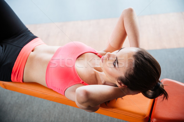 Focused sportswoman doing abs crunches on bench in gym  Stock photo © deandrobot