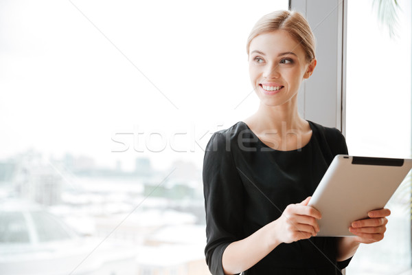 Young woman worker sitting near window while holding tablet computer. Stock photo © deandrobot