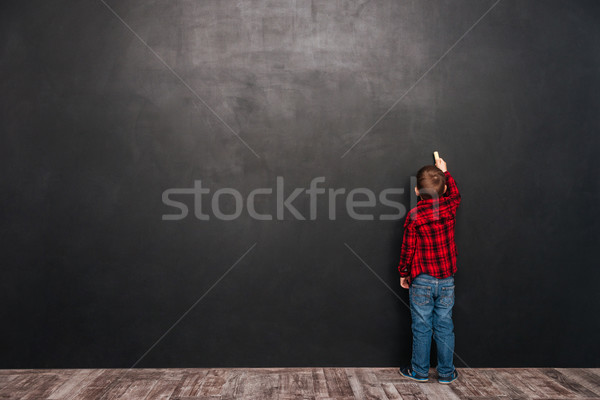 Little child standing near blackboard and drawing on it Stock photo © deandrobot