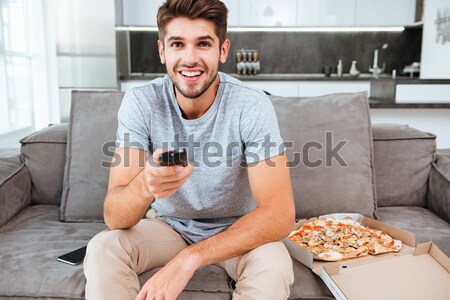 Man pushing button on remote control while holding pizza Stock photo © deandrobot