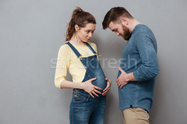 Pregnant happy woman standing near cheerful man compare stomachs. Stock photo © deandrobot