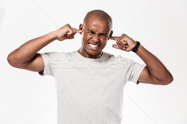 Displeased african man closes ears from a noise. Stock photo © deandrobot