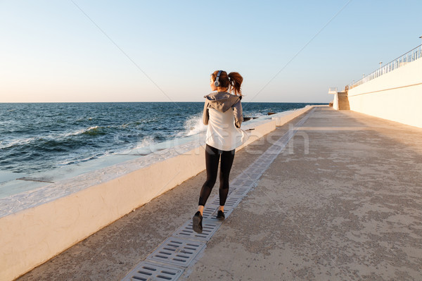 Back view of young slim fitness woman running at seaside Stock photo © deandrobot