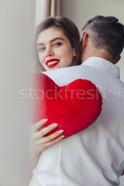 Young lady smiling and holding heart toy while hug her husband at home Stock photo © deandrobot