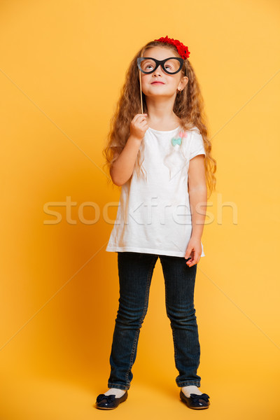 Funny little girl child holding fake glasses looking aside. Stock photo © deandrobot