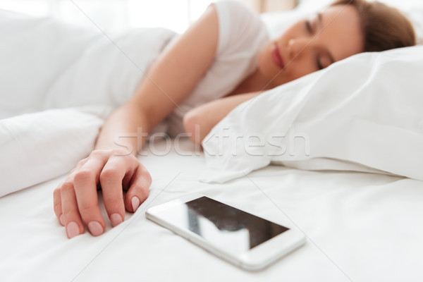 Sleeping young woman lies in bed near phone. Stock photo © deandrobot