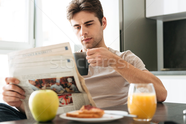 Young concentrated man reading newspaper while sitting in kitchen Stock photo © deandrobot