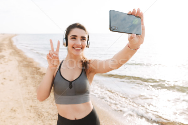 Uśmiechnięty młodych sportsmenka stałego plaży słuchawki Zdjęcia stock © deandrobot