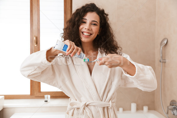 Beautiful young cute woman in bathroom brushing cleaning her teeth. Stock photo © deandrobot