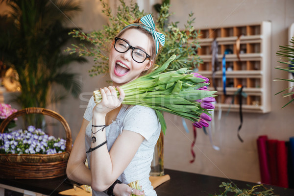 Happy woman florist holding bunch of purple tulips and winking Stock photo © deandrobot