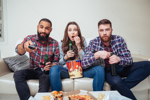 Amazed shocked friends watching tv and eating popcorn on sofa Stock photo © deandrobot