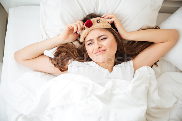 Sad woman lying on the bed with eye mask Stock photo © deandrobot