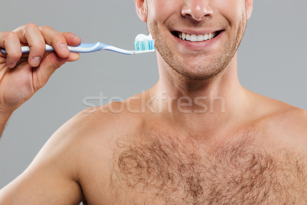 Cheerful man cleaning teeth by toothbrush with toothpaste and smiling Stock photo © deandrobot