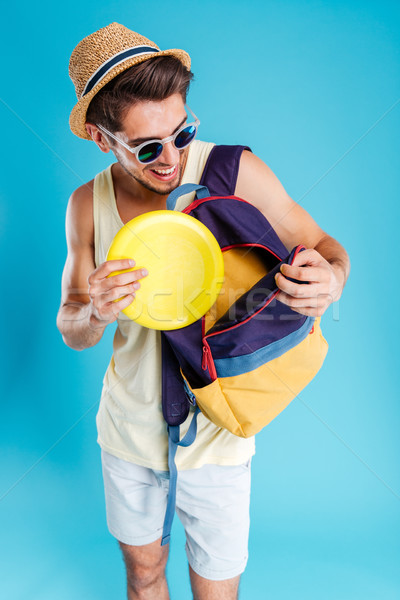 Smiling young man putting yellow frisbee disk into backpack Stock photo © deandrobot