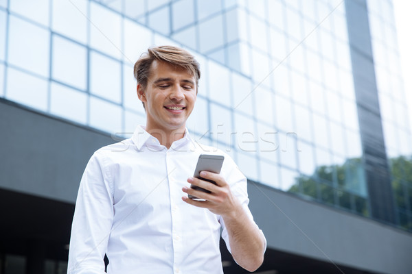 Smiling young businessman using mobile phone near business center Stock photo © deandrobot