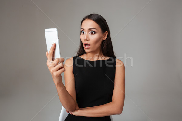 Foto stock: Mulher · jovem · vestido · preto · olhando · telefone · móvel · cinza