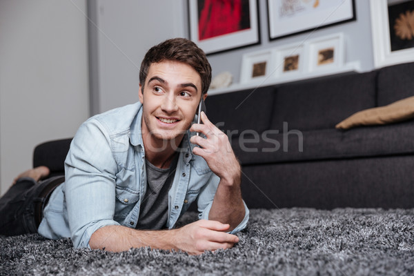 Homme tapis téléphone portable souriant jeune homme maison [[stock_photo]] © deandrobot