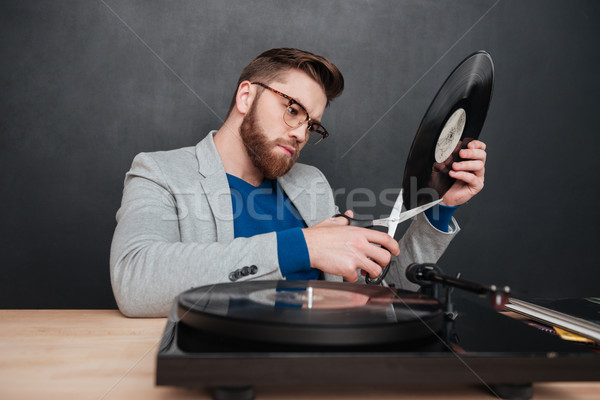 Serious young man in glasses cutting vinyl record with scissors Stock photo © deandrobot