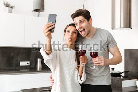 Happy loving couple standing in kitchen looking at glass. Stock photo © deandrobot