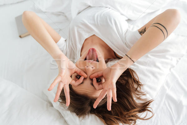 Funny woman making funny face and showing tongue in bed Stock photo © deandrobot