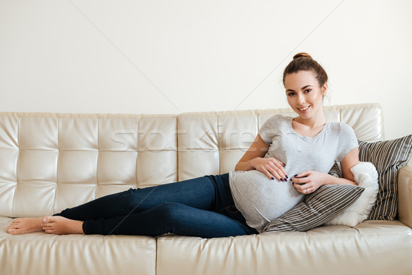 Cheerful attractive pregnant young woman lying and relaxing on sofa Stock photo © deandrobot