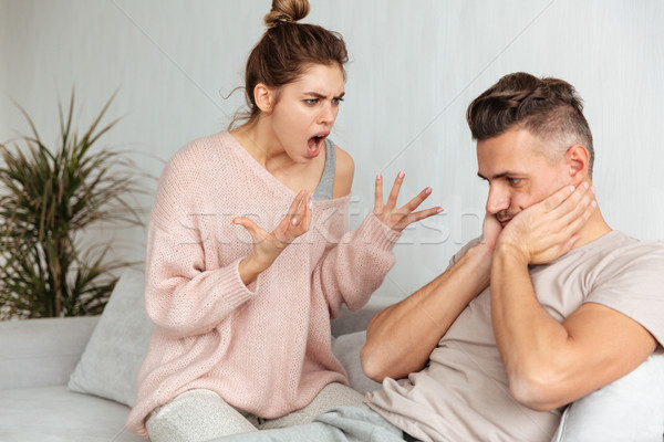 Confused man sitting on couch with him girlfriend which screaming Stock photo © deandrobot