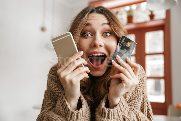 Happy emotional woman 20s holding credit card and mobile phone,  Stock photo © deandrobot