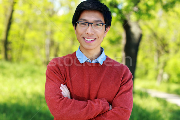 Cheerful asian young man standing with arms folded in a park Stock photo © deandrobot