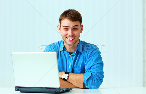Young smiling casual businessman in blue shirt sitting at the table in office Stock photo © deandrobot