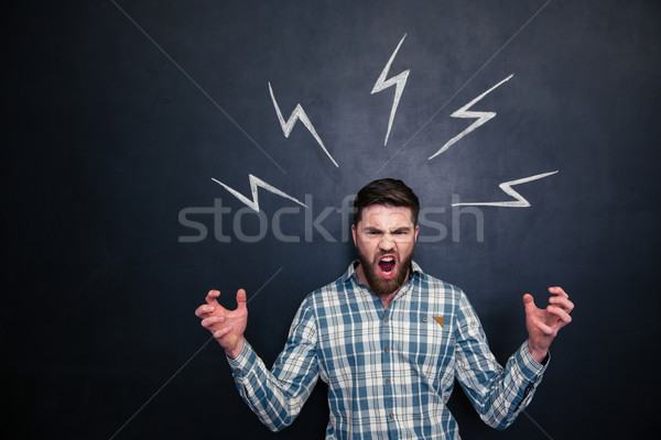 Crazy man shouting and standing under drawn lightnings over blackboard  Stock photo © deandrobot