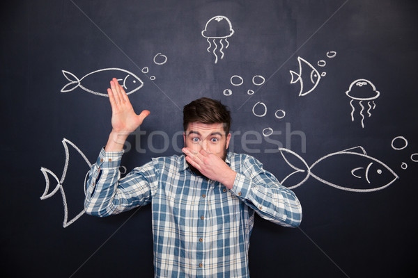 Amusing man imitating diving in ocean over blackboard with drawings Stock photo © deandrobot