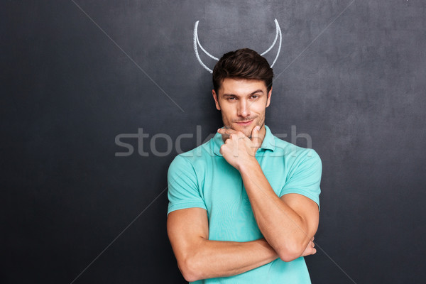 Thoughtful man pretending devil standing over chalkboard with drawn horns Stock photo © deandrobot
