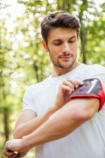 Man athlete standing and using smartphone in handband at forest Stock photo © deandrobot