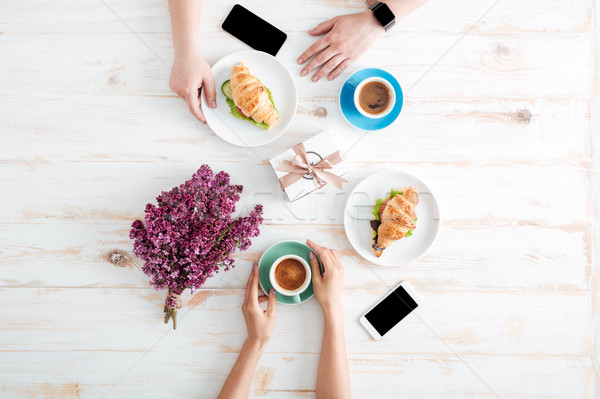 Hands of couple drinking coffee and eating croissants on table Stock photo © deandrobot