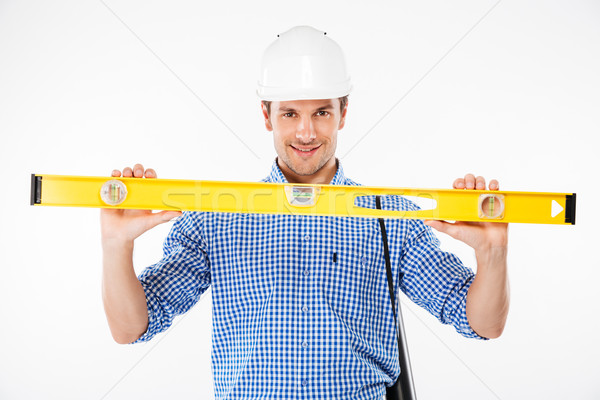 Happy young man builder in building helmet holding spirit level Stock photo © deandrobot