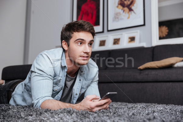 Man lying on a carpet and using mobile phone Stock photo © deandrobot