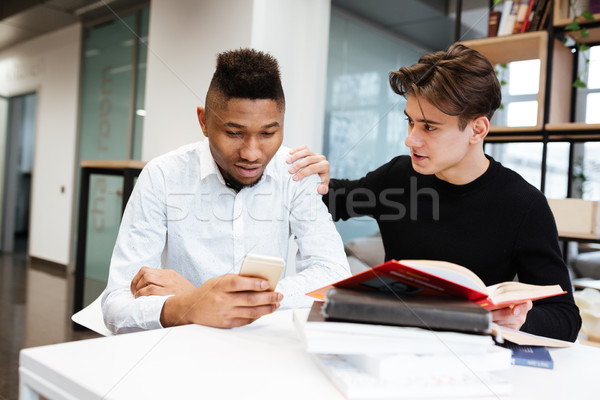 Two young students in library choose between book and cellphone. Stock photo © deandrobot