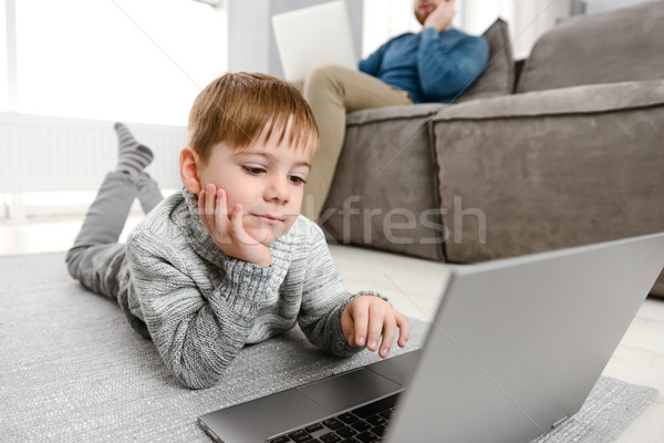 Cheerful child using laptop while lies in floor Stock photo © deandrobot