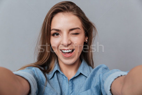 Smiling Woman in shirt making selfie in studio and winks Stock photo © deandrobot