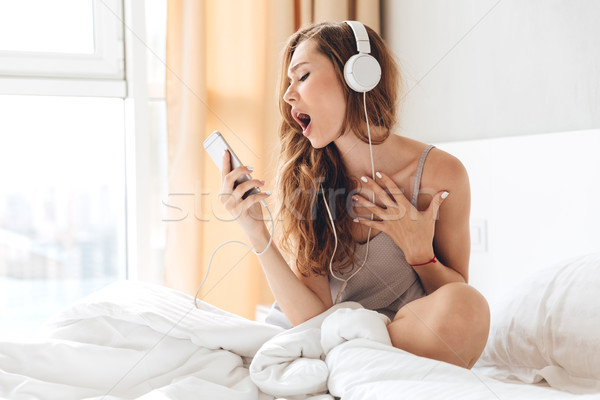 Young woman listening music and singing in bed Stock photo © deandrobot