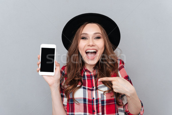 Excited casual woman pointing finger at blank screen mobile phone Stock photo © deandrobot
