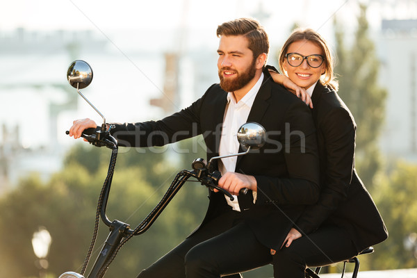 Side view of smiling couple in suits rides on motorbike Stock photo © deandrobot