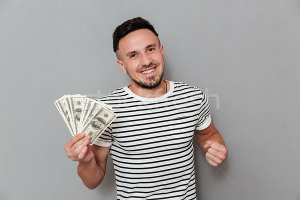 Happy man in t-shirt holding money and looking at camera Stock photo © deandrobot