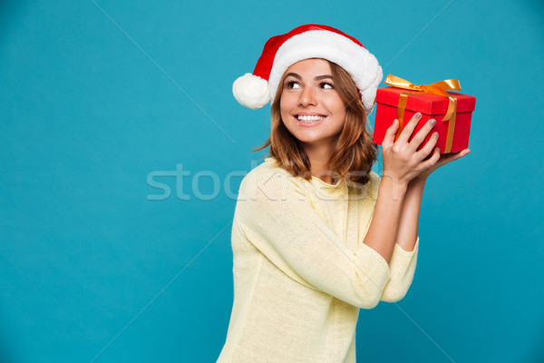 Smiling intrigued woman in sweater and christmas hat holding gift Stock photo © deandrobot