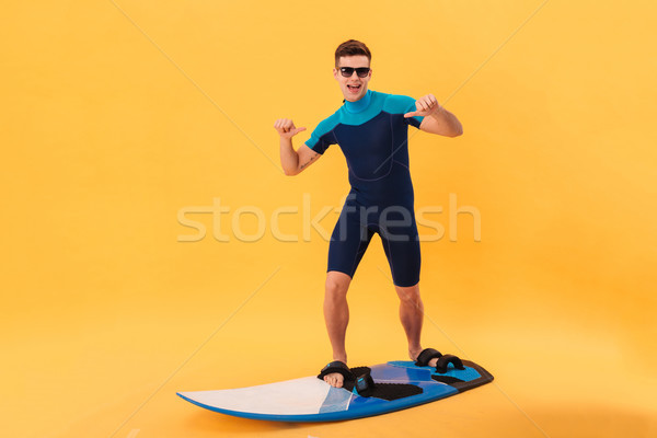 Cheerful surfer in wetsuit and sunglasses using surfboard Stock photo © deandrobot
