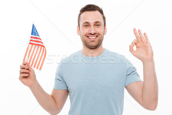 Photo of joyful young man in casual t-shirt holding small americ Stock photo © deandrobot